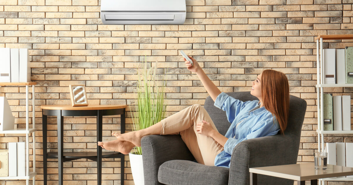 Young woman switching on air conditioner while sitting in armchair at home