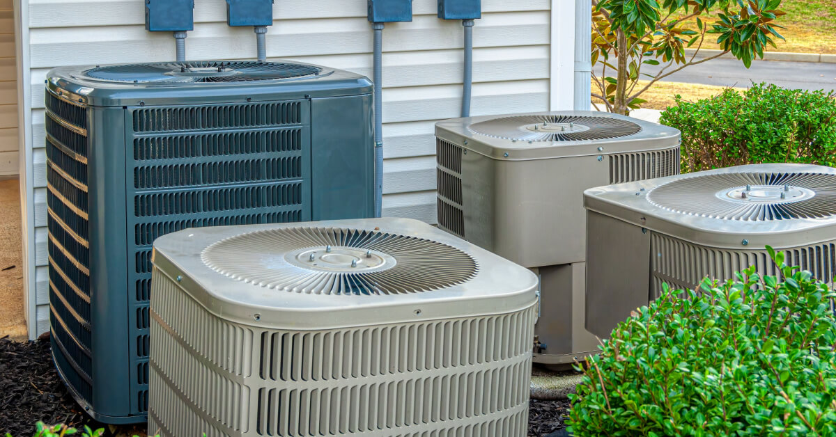 Horizontal shot of four air conditioning units outside of an upscale apartment complex.